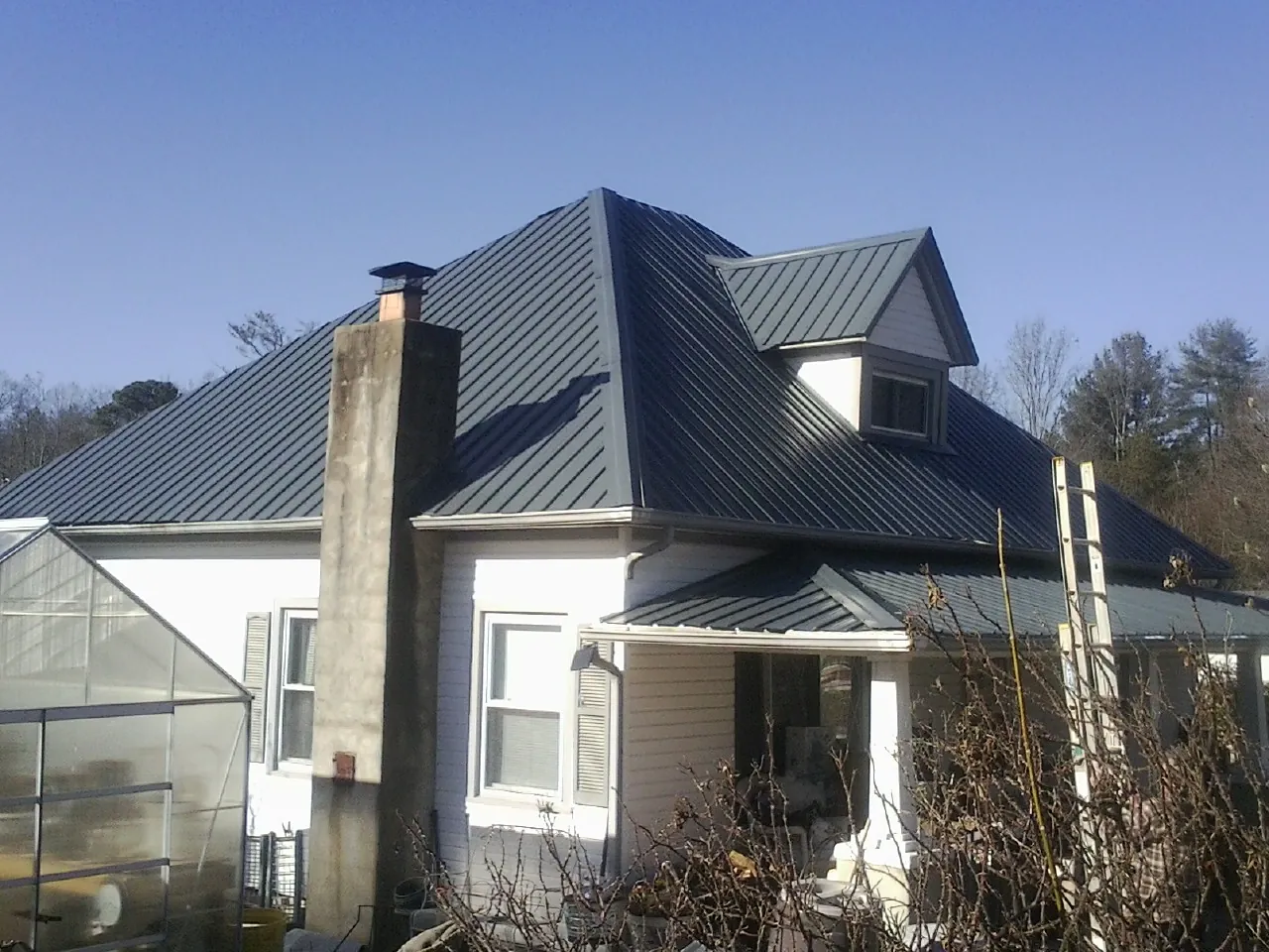 Dark blue standing seam metal roof on a white farmhouse with dormer — Slate & Tile Roof Repair by Roofing Brothers in Auburndale