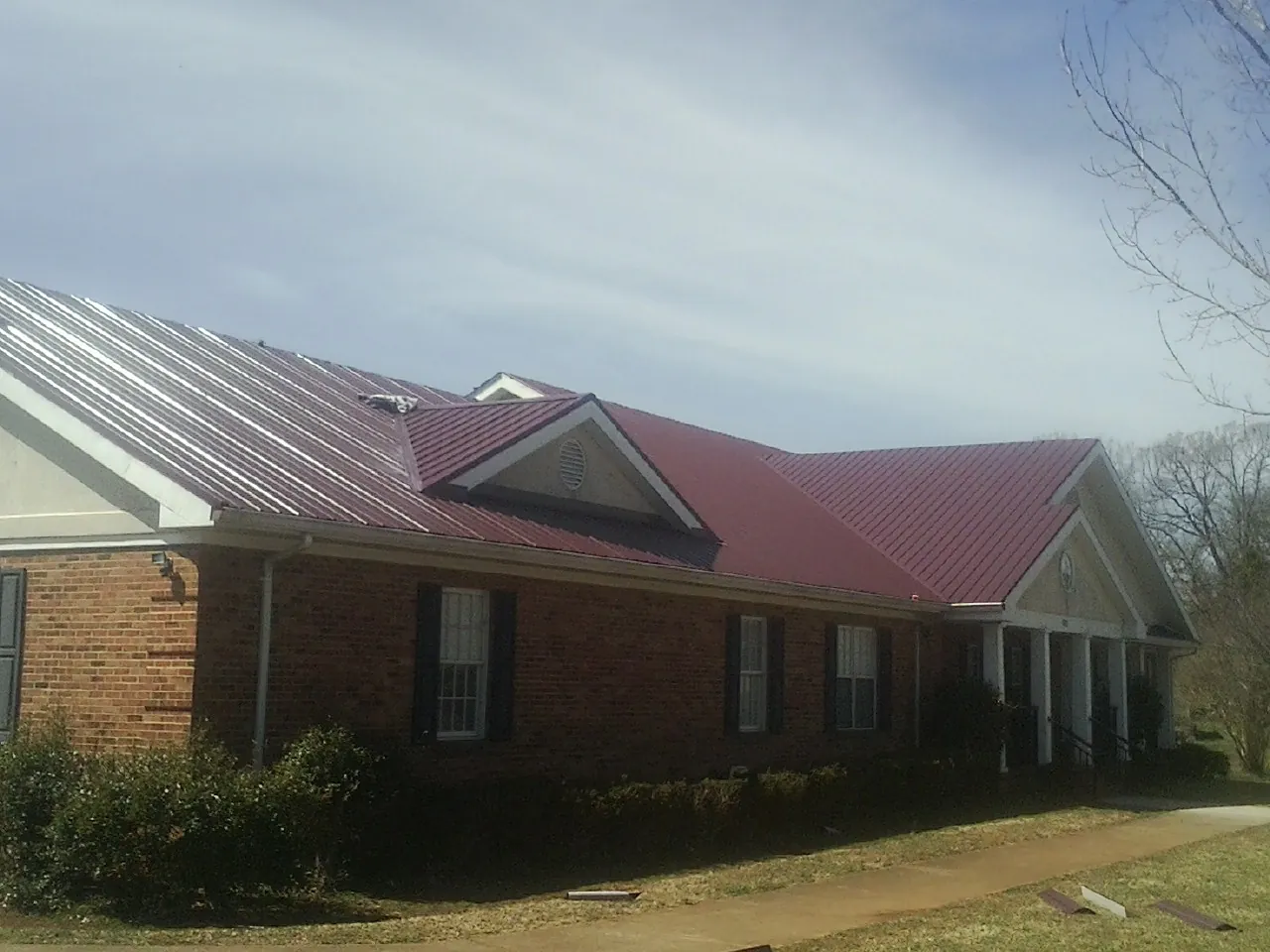 Red metal roof with gabled entries on a long brick building, from a Hail Damage Roof Repair job in Auburndale